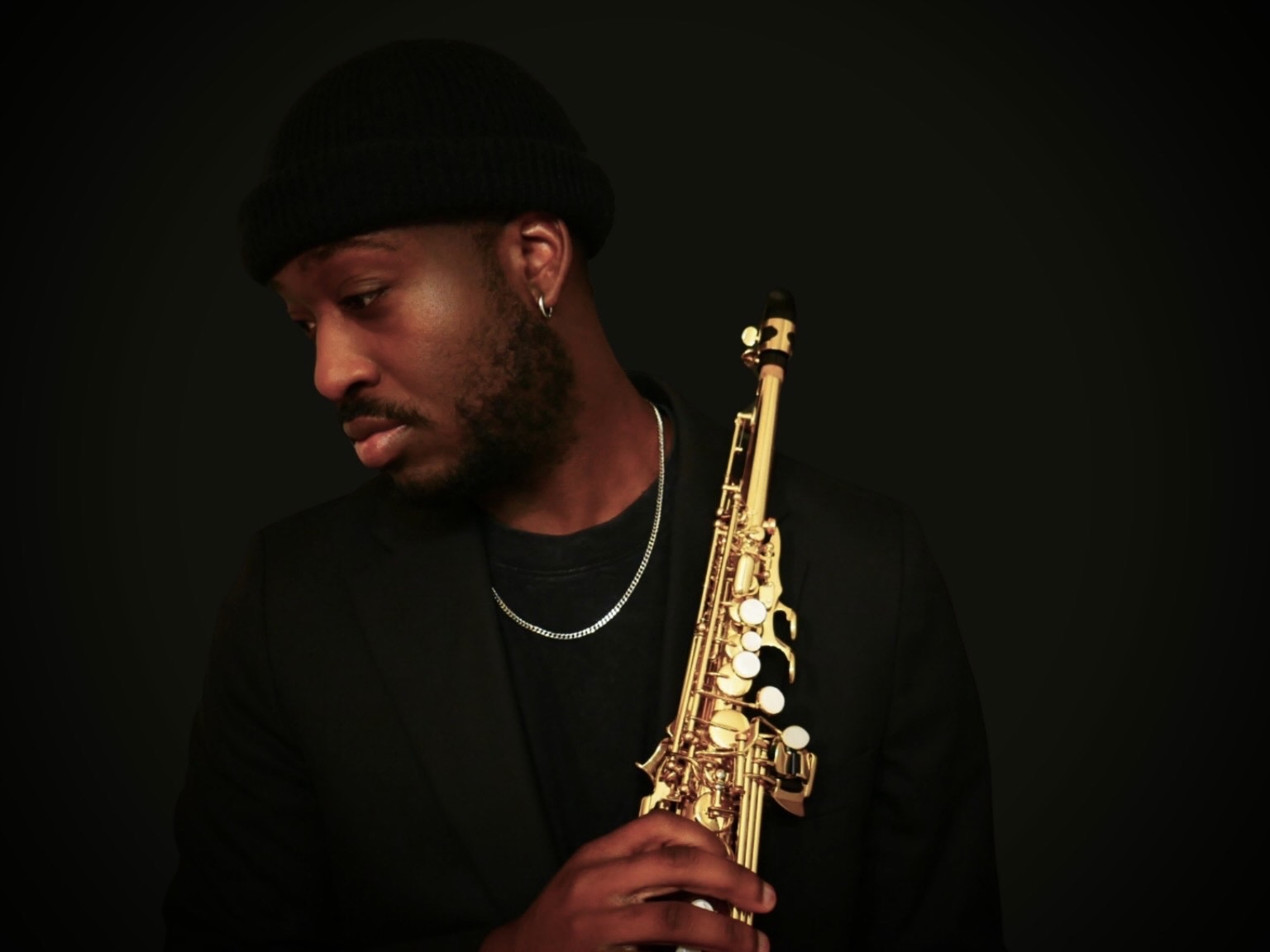TAVE holding his saxophone, wearing a black hat